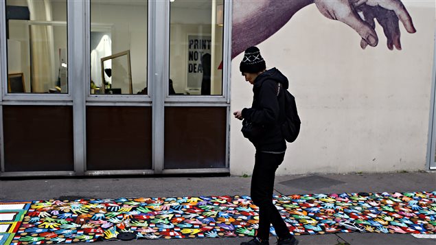 Une femme photographie une bannière avec des mains en couleur devant les locaux de Charlie Hebdo, à Paris. Une femme photographie une bannière avec des mains en couleur devant les locaux de Charlie Hebdo, à Paris.
