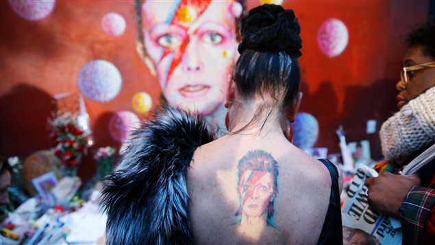 À Londres, une femme arbore un tatouage de Ziggy Stardust devant une murale représentant le personnage qu'incarnait David Bowie, où a grandi la légende du rock. À Londres, une femme arbore un tatouage de Ziggy Stardust devant une murale représentant le personnage qu'incarnait David Bowie, où a grandi la légende du rock.