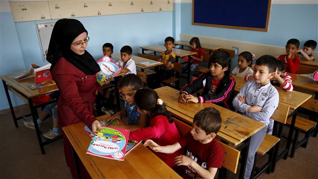  A Syrian refugee teacher distributes books to her refugee students in their classroom at Fatih Sultan Mehmet School in Karapurcek district of Ankara, Turkey, September 28, 2015.