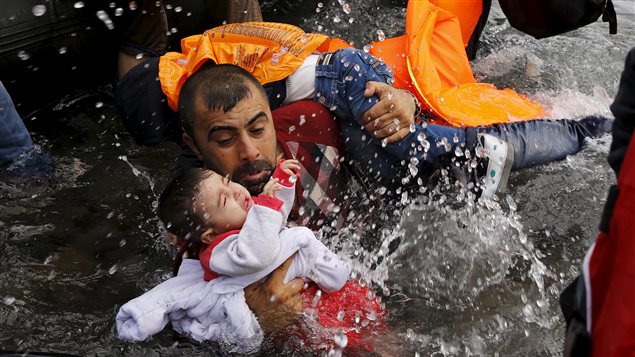  A Syrian refugee holds onto his children as he struggles to walk off a dinghy on the Greek island of Lesbos, after crossing a part of the Aegean Sea from Turkey to Lesbos, September 24, 2015.