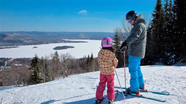 Un père et sa fille se préparent à descendre une pente de ski.