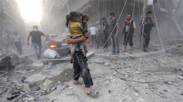 شاب يحمل طفلتين سوريّتين وسط الدمار في حلب بعد تعرّضها للقصف على يد قوّات النظام في  9-7-2014