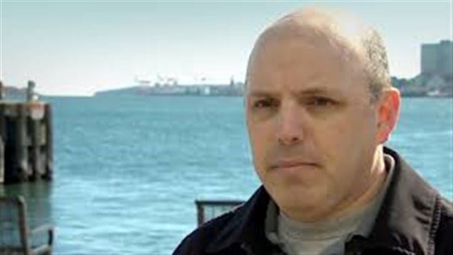 Retired Sub-Lieutenant Paul Ritchie continues his battle with the Canadian Military. We see a man from the neck up with the Halifax harbour in the background. He is balding and carries a look of determination on his face.