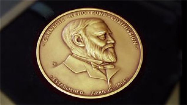The Carnegie Medal honours great civil bravery. We see a gold, round medal with Carnegie's face imprinted on it. He wears an old-fashioned jacket, close-cropped hair and a full beard.