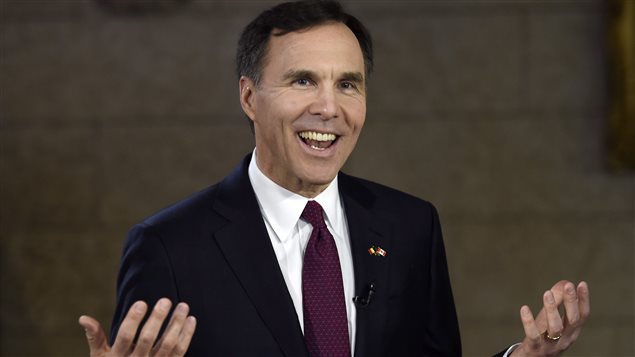 Minister of Finance Bill Morneau hopes happy days are ahead for the Canadian economy. We see Morneau is a sharp, dark suit. He gestures with both hands held open and sports a wide smile. He is a tall, dark-haired man, immaculately coifed, with a beautiful set of very white teeth.