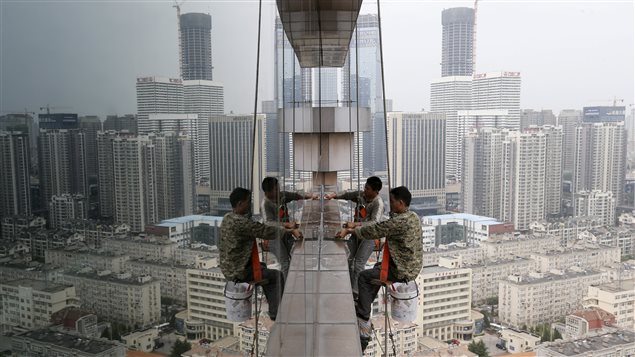 Des travailleurs nettoient les fenêtres en verre d’un bâtiment de 30 étages à Qingdao, en Chine.