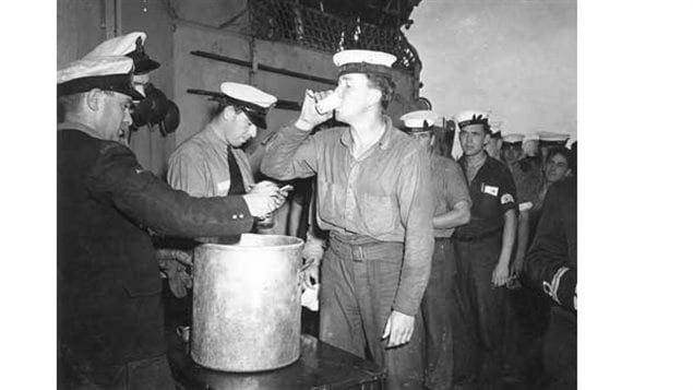 Ordinary Seaman Ernest Weir receives an extra rum ration during Victory over Japan celebrations aboard HMCS Prince Robert, Sydney, Australia, 16 Aug 1945