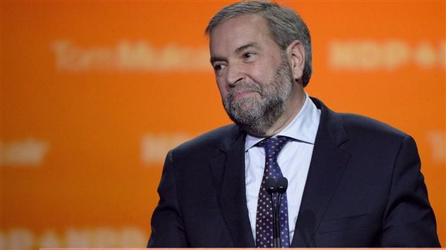 NDP Leader Tom Mulcair speaks to supporters on election night, Oct. 19, 2015, in Montreal, after the party failed to live up to optimistic predictions. Mulcair stands in front on an orange wall. A bearded man with salt-and-pepper hair, he is dressed immaculately in a blue suit and blue tie. His wears a weary and sad expression.