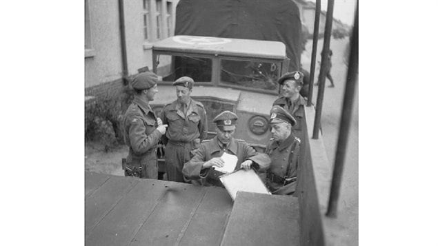 British and German officers standing between Canadian designed and built CMP 60cwt trucks, sign the truce deal on 12 April 1945