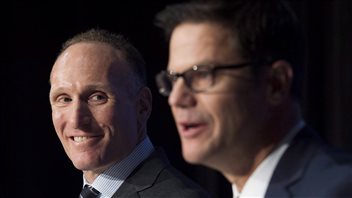 Blue Jays president and CEO Mark Shapiro, left, was smiling in December when he introduced new general manager Ross Atkins. It's unlikely either man is having a barrel of laughs watching the team play this season. Both are dressed in fancy grey suits. Shapiro, whose hair is receding (he appears to be trying to compensate with a weave, but it's difficult to tell) has a slightly crooked grin across his mouth as he listens to Atkins, who has short hair and wears black-rimmed glasses, address the press.