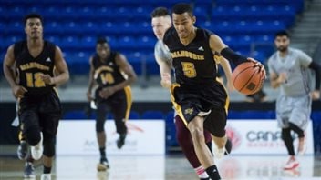  Few were in the stands to watch Dalhousie upset Ottawa at the CIS men's basketball championship quarter-finals this spring in Vancouver. CIS officials are looking for ways to attract bigger crowds. We see a young black man dribbling with his left hand, wearing a black uniform with yellow writing spelling Dalhousie on the chest. He is leading a charge down the court, trailed by two teammates and two Ottawa players wearing light blue uniforms.