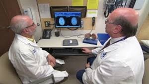 Dr. Mark Freedman, right, and Dr. Harold Atkins have worked closely together for the past 13 years on a stem-cell clinical trial to treat MS in patients with an incurable form of the disease. We see the two men from the side wearing their lab coats and studying a medical machine on a desk in front of them. Dr. Freedman is large and balding. Dr. Atkins is slim and greying.