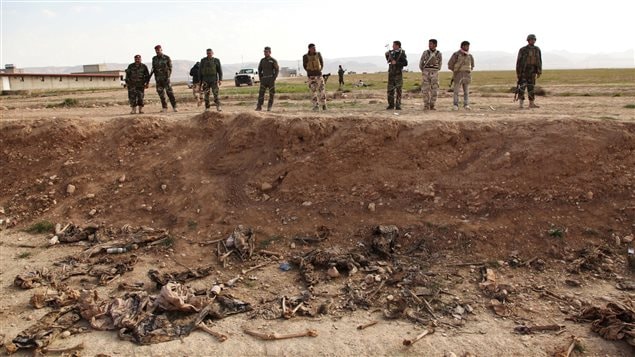  Kurdish peshmerga forces look at bones in a mass grave on the outskirts of the town of Sinjar, February 3, 2015.