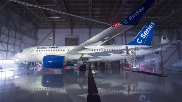 A Bombardier CSeries jet is seen in a hangar in Montreal in February. It's a lovely shot, actually. We see the whole plane in a long shot from the side. It's jet engines are painted a bright blue as the tail and wing tips. CSeries is written on the blue while Bombardier is written on the plane's size. The plane's main body is white and gleaming. If fact, the whole plane is gleaming and is reflected in the floor below.