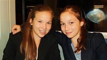 Emma, right, and Julia Mogus in 2012 when they created 'Books With No Bounds.' Emma has her right arm around her. Both have gorgeous, freshly washed long, light brown hair. Both are wearing dark sports jackets. Julia smiles through a full set of braces.