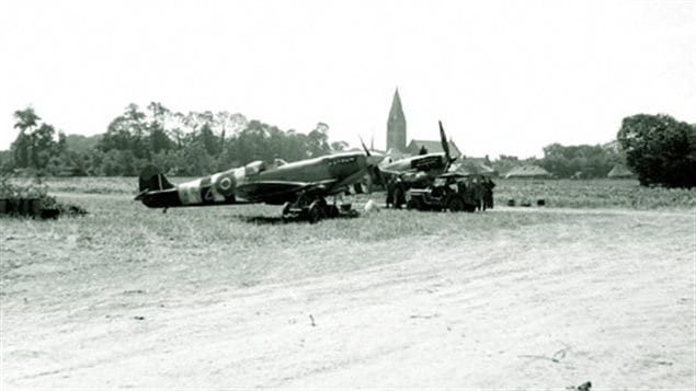 RCAF 412 Squadron Spitfires at their base in Beny-sur-Mer operating from a makeshift dir airstrip. Note the D-Day paint scheme -black and white stripes on the planes. The lead plane is a MkIX with 4-blade prop and 20mm wing cannon.