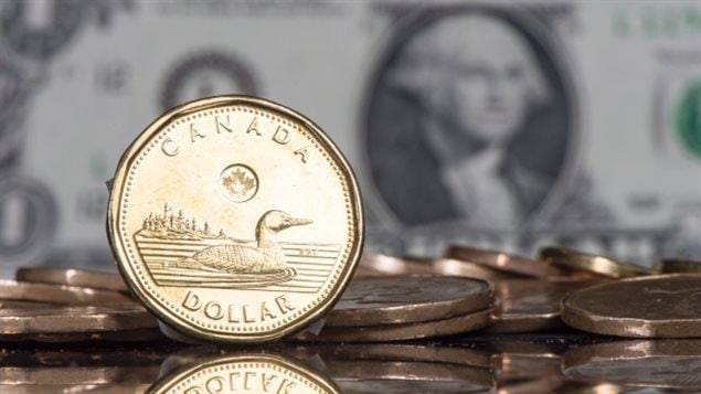 More than a billion of Robert-Ralph Carmichael's loonie coins have been minted since 1987. We a polished, golden coin sitting on his rim in front of others that are flat on a table. For a bit of perspective we see a U.S. paper one-dollar bill in the background with George Washington looking back at us.