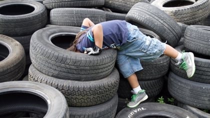 Skill testing question: What is this kid looking for? We see a pre-teen kid wearing jeans that stop at the knee and a blue tee shit. His head is buried in the hole of a top tire of a pile of tires at a dump filled with more tires.