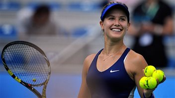Canadian tennis fans are hoping Genie Bouchard can re-ignite her flagging career in her hometown next week. We see Genie dressed in blue on the practice court with an enormous smile on her face. She holds a racket in her rear right hand and four yellow tennis balls in her left hand.