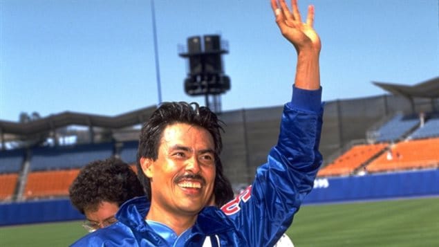 Dennis Martinez at Dodger Stadium in Los Angeles on July 28, 1991, after pitching the 13th perfect game in major league baseball history. We see Dennis from the shoulders up. He wears a wide smile on his face as he waves with his left hand.