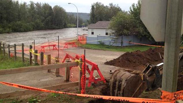 Recovering the fire that the struck the city in May, residents of Fort McMurray are now dealing with flooding from massive rains. We see a show of some small houses. They are surrounded by red police lines and a flooded street running between the houses and evergreen trees on the other side.