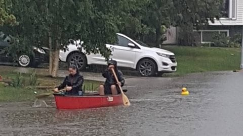  Already grappling with the after-effects of last spring's wildfire, residents of Fort McMurray, faced new problems on the last Saturday of July when 85 millimetres of rain fell in two hours. We see two people in a red canoe paddling down a residential street. A white SUV sits in a driveway behind them.