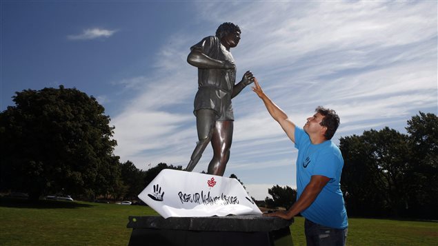 Conrad Burns connects with the statue of Terry Fox in Victoria, B.C. on Monday after completing his walk from St. John's, N.L. to create awareness about abuse and violence. Under a blue sky filled with wispy cirrus clouds, Burns (on the right) wearing a blue tee-shirt reaches up with his right hand to touch the left hand of the statue.