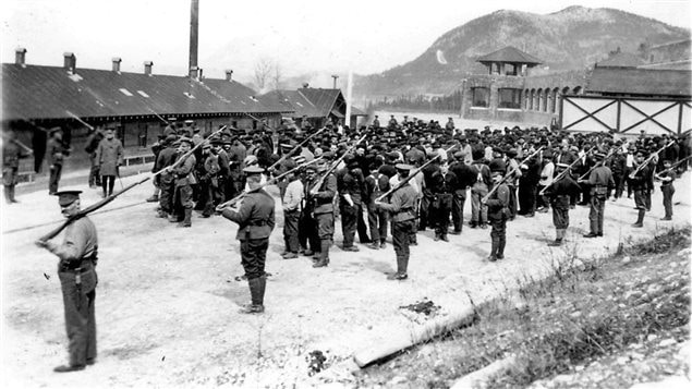 Guards watch over the mostly Ukrainian prisoners at the internment camp at the Cave and Basin site at Banff Alberta in World War I, During both world wars, about two dozen internment camps were set up across Canada, which often involved forced labour. While several thousand *enemy aliens* were interned, many thousands of others were left at large but required to report regularly to police.