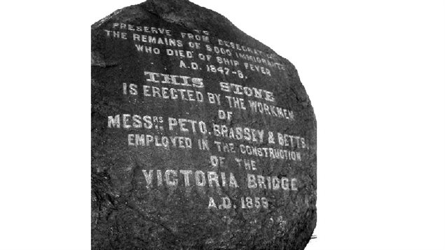 Photo of the large black rock placed near the entrance to the bridge to commemorate the Irish immigrants whose remains were discovered during excavations for the bridge. The Irish immigrants had died during a typhus epidemic in *fever sheds* near the site.