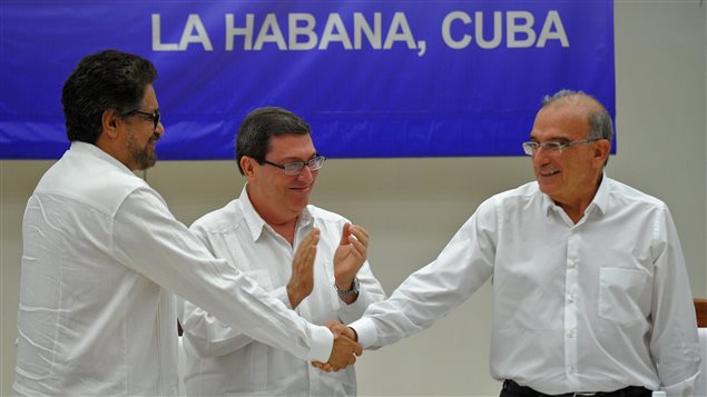 Humberto de la Calle (der) jefe negociador del gobierno colombiano e Iván Márquez, jefe negociador de las FARC (izq), se aprietan la mano bajo la mirada complacida de Bruno Rodríguez, ministro cubano de Relaciones Exteriores.