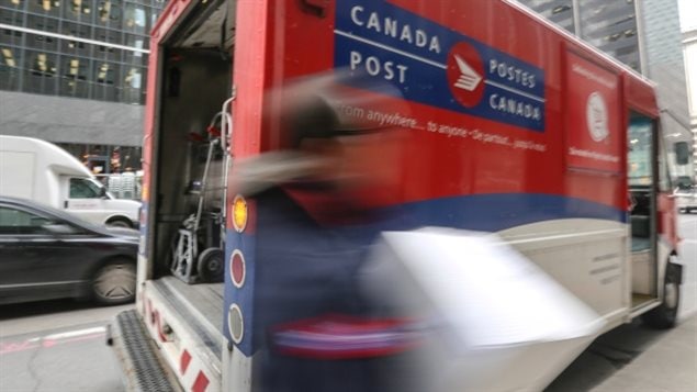 It appears it is now full-speed ahead for postal service across Canada. We see a big red and blue mail van on a city street with an (arty) blurred shot of a postal worker carrying a package next to it