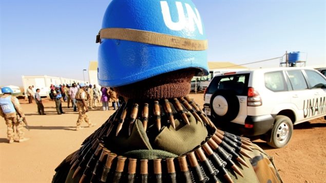 Canadian peacekeepers could be headed to Mali. We see a soldier from the back. He wears a UN blue helmet and has bullets wrapped around his shoulders and neck. In the distance is a white UN SUV.
