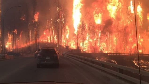 This spring's wildfires near Fort McMurray drove the Canadian economy a good distance south. We see a car making its way down a road that is surrounded on both sides by giant flames.