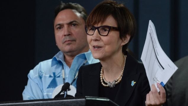 Assembly of First Nations National Chief Perry Bellegarde looks on as First Nations Child and Family Caring Society of Canada's Cindy Blackstock speaks about the Canadian Human Rights Tribunal on discrimination against First Nations children in care, during a news conference in Ottawa in January. Darked-haired and intense, Blackstock, dressed in black and wearing dark glasses, is seen in the right of the photo leaning forward and holding a peace of paper in her left hand as he speaks into a microphone. Bellegarde sits behind her, wearing a dress shirt and calm expression on his face. 