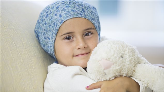 Une petite fille avec un foulard bleu sur la tête assise avec une peluche dans les bras. 