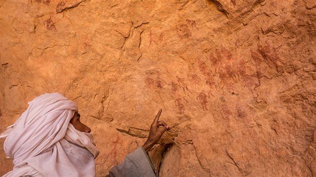  Yahia Salah Muftah, a local driver points at ancient drawings showing a group of figures on the wall of the Wan Amel cave in Wadi Tashwenat in Libya’s Akakus mountain region, in the desert of the western Ghat District, on January 1, 2016. 