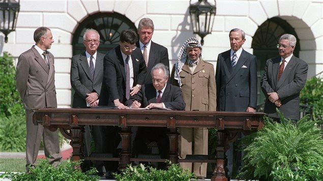 Le ministre des Affaires étrangères d’Israël, Shimon Peres, signe l’accord d’Oslo lors d’une cérémonie à la Maison-Blanche, à Washington, le 13 septembre 1993, en présence, entre autres, du ministre russe des Affaires étrangères, du premier ministre israélien Itzhak Rabin, du président américain Bill Clinton, de Yasser Arafat, du secrétaire d’État américain Warren Christopher et du directeur de l’OLP Mahmoud Abbas.