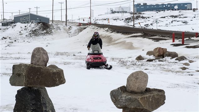 Un homme conduit une motoneige devant deux inukshuks à Iqualuit, Nunavut