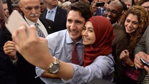 Justin Trudeau, entouré de partisans et d’un garde du corps, prend un égoportrait avec une femme musulmane souriante. 