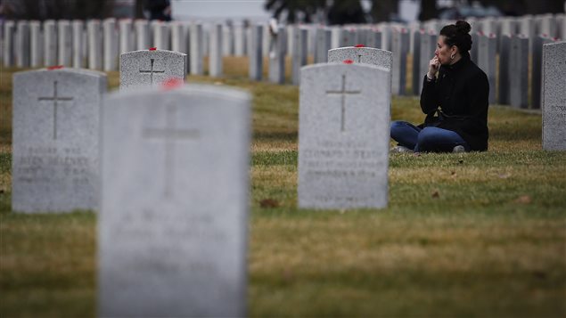 A woman sits beside a grave marker at a military cemetery following a Remembrance Day service in Calgary, Friday, Nov. 11, 2016.