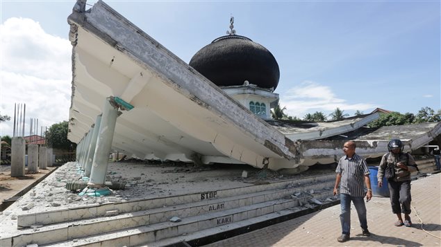 People walk near a collapsed mosque following an earthquake in Meuredu, Pidie Jaya in the northern province of Aceh, Indonesia December 7, 2016 in this photo taken by Antara Foto.