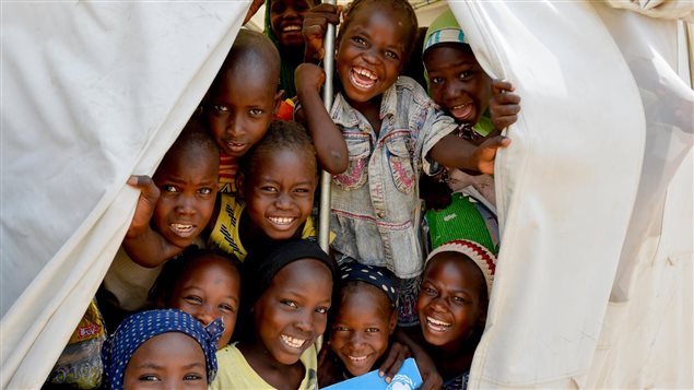 Niños a la entrada de una carpa del Unicef donde asisten a clases y reciben un cuaderno de ejercicios.