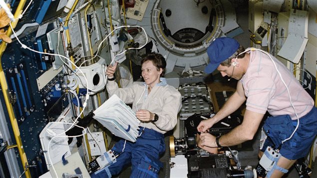 Roberta L. Bondar, payload specialist works at the International Microgravity Laboratory’s (IML-1) biorack while astronaut Stephen S. Oswald, pilot, changes a film magazine on the IMAX camera. The two were joined by five fellow crew members for 8-days of scientific research aboard the Space Shuttle Discovery in Earth-orbit. Most of their on-duty time was spent in this IML-1 Science Module, positioned in the cargo bay and attached via a tunnel to Discovery’s airlock