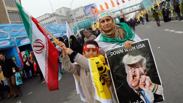Una mujer sostiene un cartel que muestra el presidente de Estados Unidos, Donald Trump, golpeado por una persona que lleva una pulsera con los colores de la bandera iraní. 
