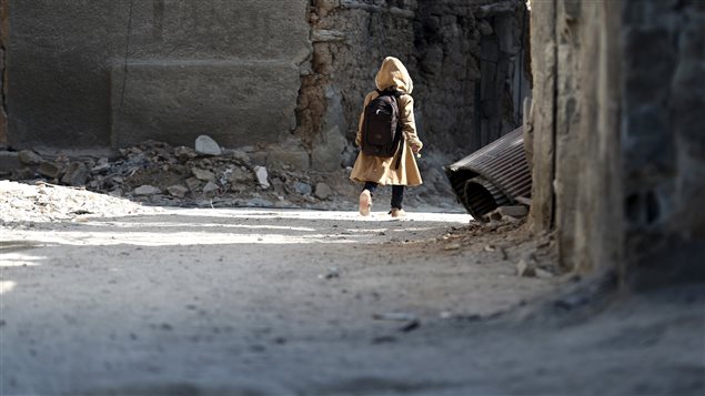 A child carries a school bag near damaged buildings in Harasta, in the eastern Damascus suburb of Ghouta, Syria January 30, 2016. About 1.7 million children are not attending school in Syria because of the war.