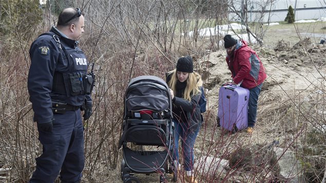 An RCMP officer watches this as a pair of asylum seekers and their baby, claiming to be from Syria, cross the border into Canada from the United States this past Monday near Hemmingford, Que. A growing number of people have been walking across the border into Canada to claim refugee status. 