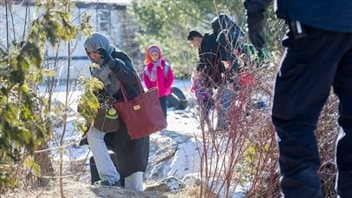 Un agent de la GRC regarde une famille qui prétend être originaire du Yémen traverser la frontière entre les États-Unis et le Canada à Hemmingford (Qc), dimanche. (Graham Hughes / Presse canadienne)