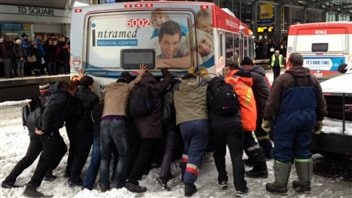 Des usagers du transport en commun de Calgary joignent leurs forces pour pousser leur bus hors de la neige - CBC