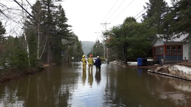 Les pompiers et les résidents évaluent les inondations sur le Chemin de la Rivière à Val-Morin, situé dans les Laurentides. (Sudha Krishnan / CBC)