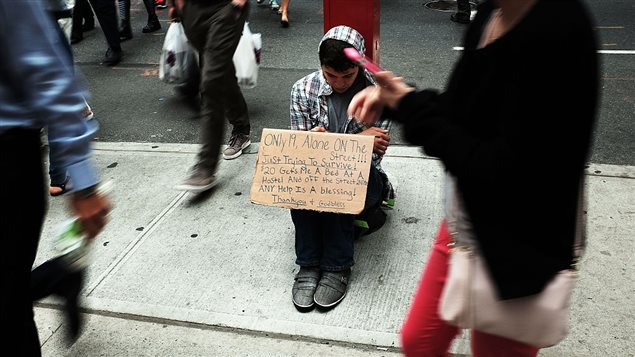 Un joven pide dinero en una calle de una gran ciudad. El afiche dice en parte *Sólo 19 años, solo en la calle. Estoy tratando de sobrevivir...*